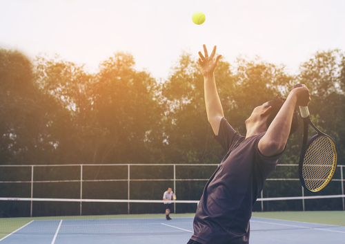 A man partaking in the physical activity pyramid by serving up a tennis ball to a friend