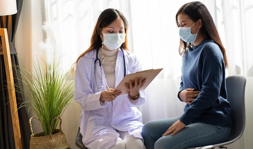 Female doctor explaining IBD awareness to a female patient clutching her stomach