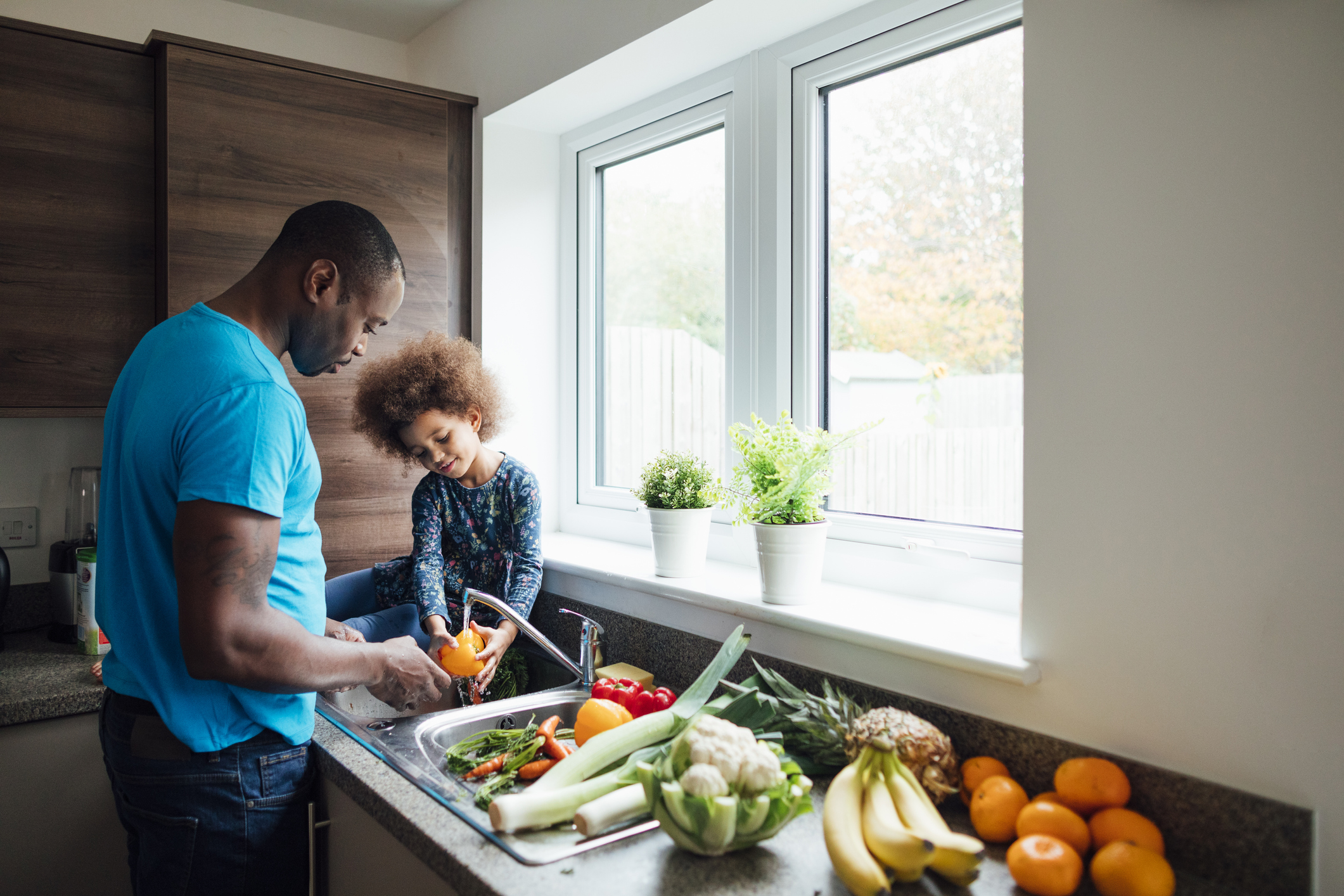 Father and daughter taking part in nutrition services rinsing off vegetables in the kitchen