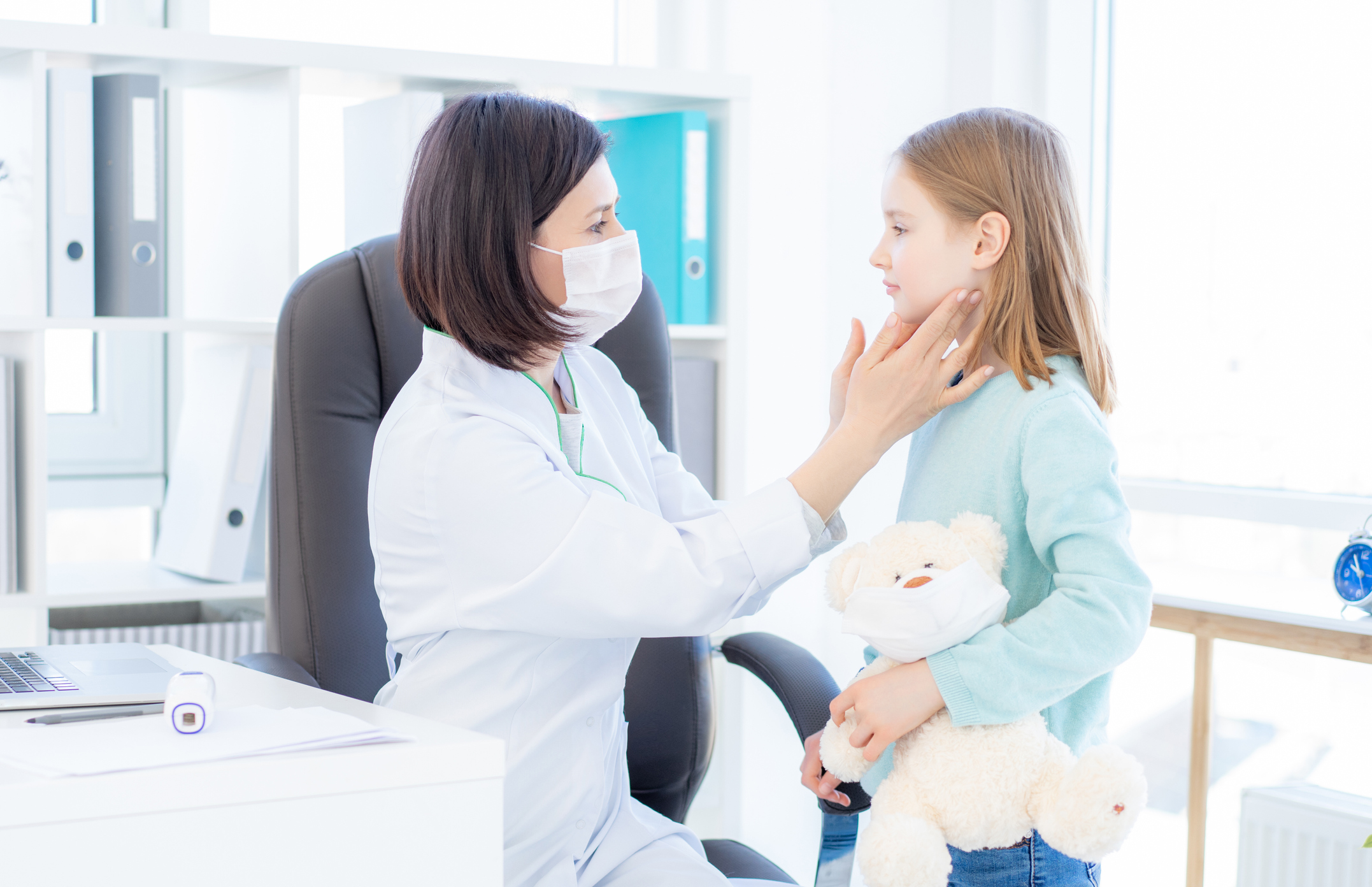 Masked doctor examining a young patient for infectious mononucleosis symptoms through swollen lymph nodes