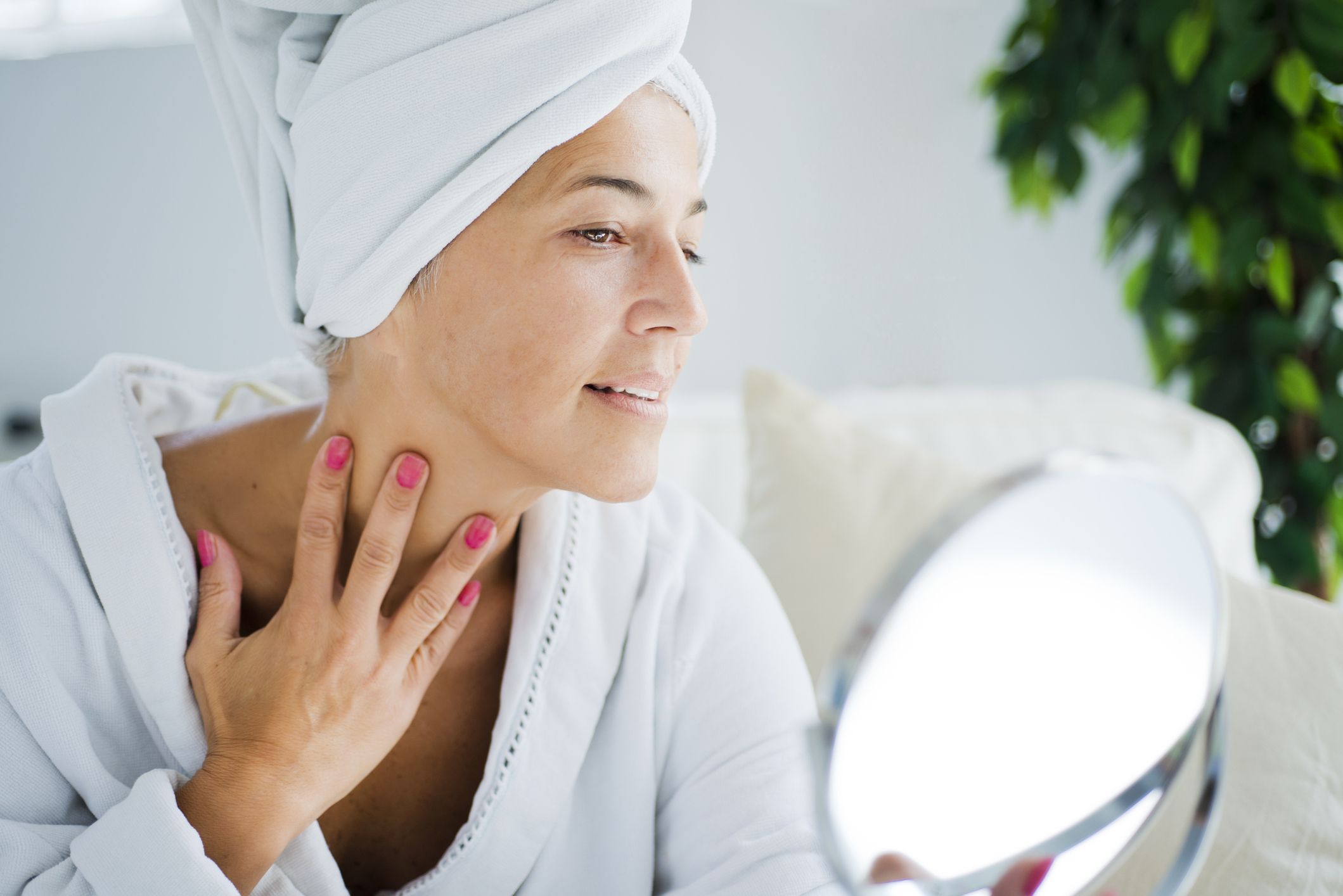 Beautiful mature woman applying a cream on her face and neck after showering