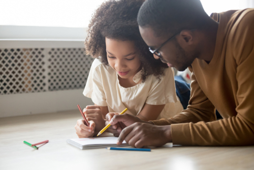A young child drawing with her father during the COVID-19 pandemic
